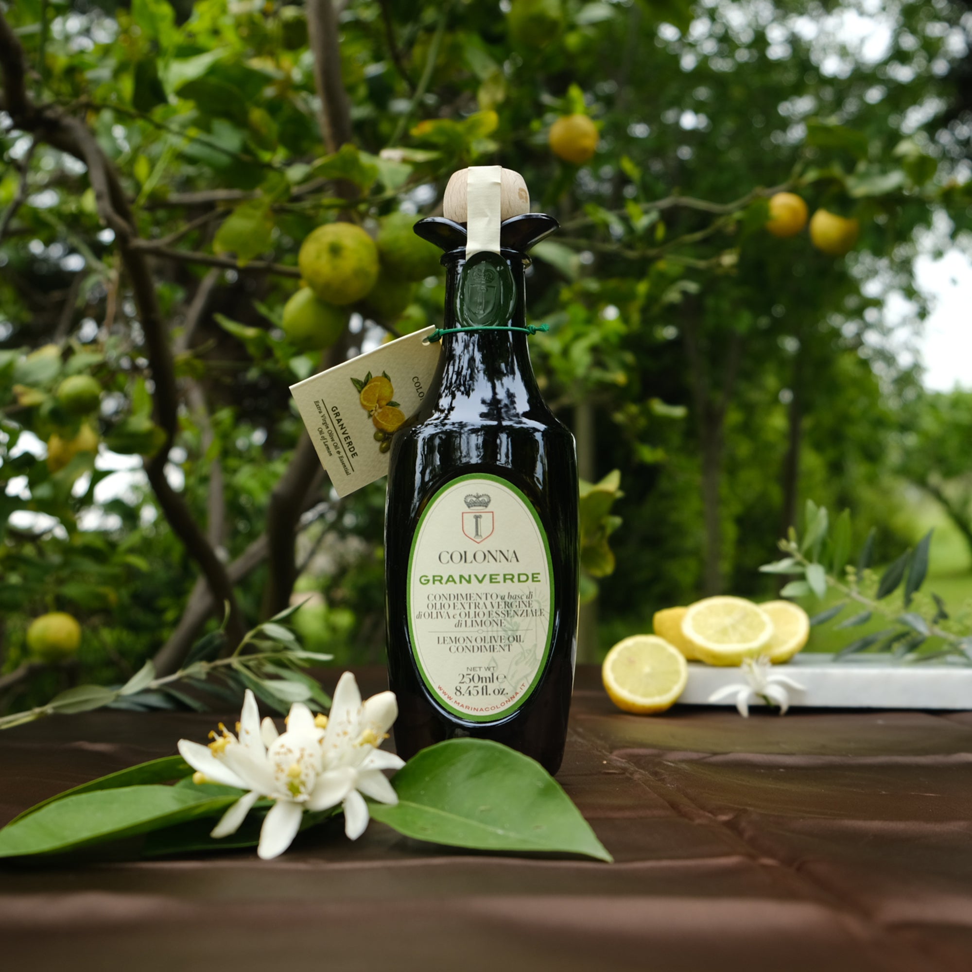 Colonna Granverde Lemon 250 ml bottle among fresh lemons, citrus blossoms, and leafy branches.