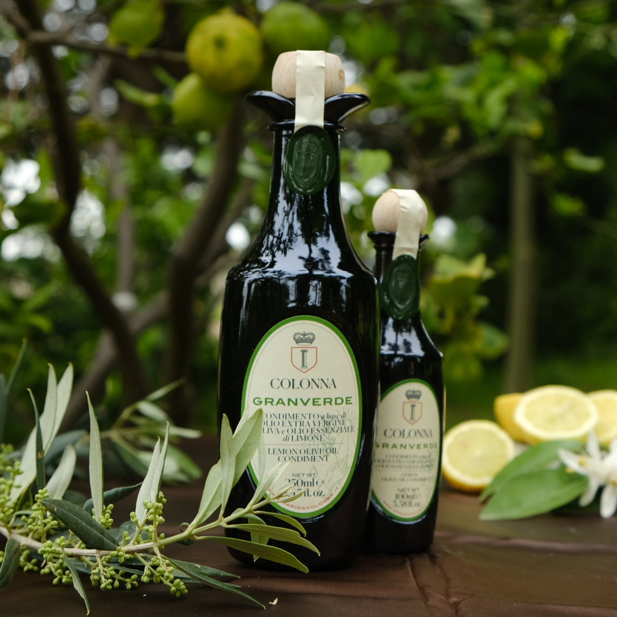Colonna Granverde Lemon bottles beside lemons, olive branches, and citrus blossoms.