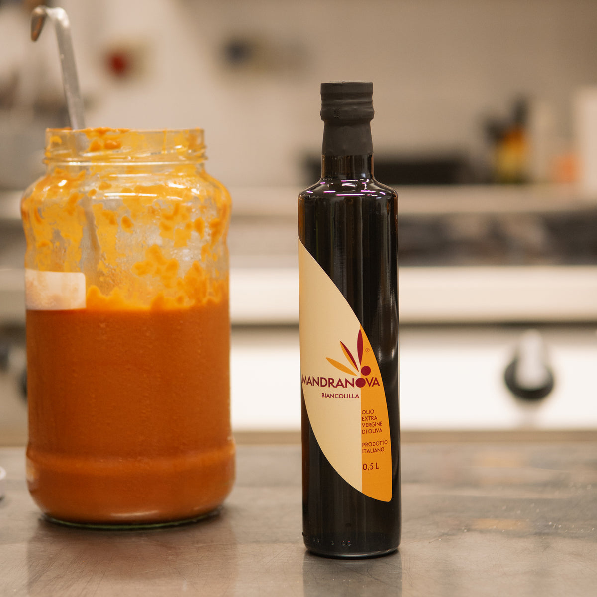 Mandranova Biancolilla 500 ml bottle beside a large jar of orange sauce in a kitchen.