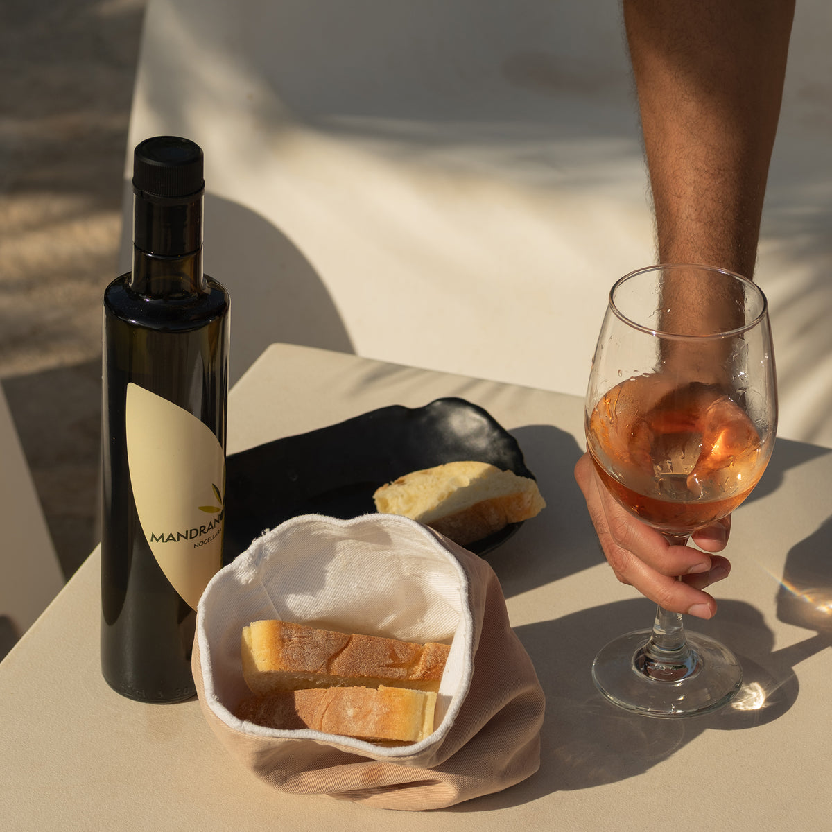 A 500 ml bottle of Mandranova Nocellara beside bread and a person holding a glass of rosé wine.