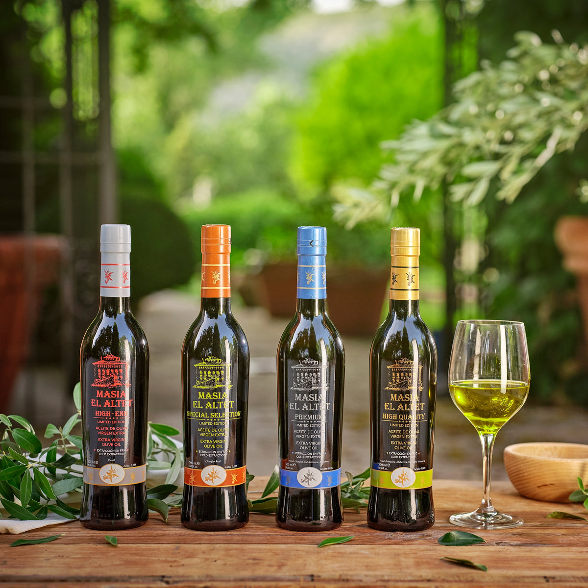Four 500 ml Masia El Altet olive oils on a table with olive branches and a glass of olive oil.