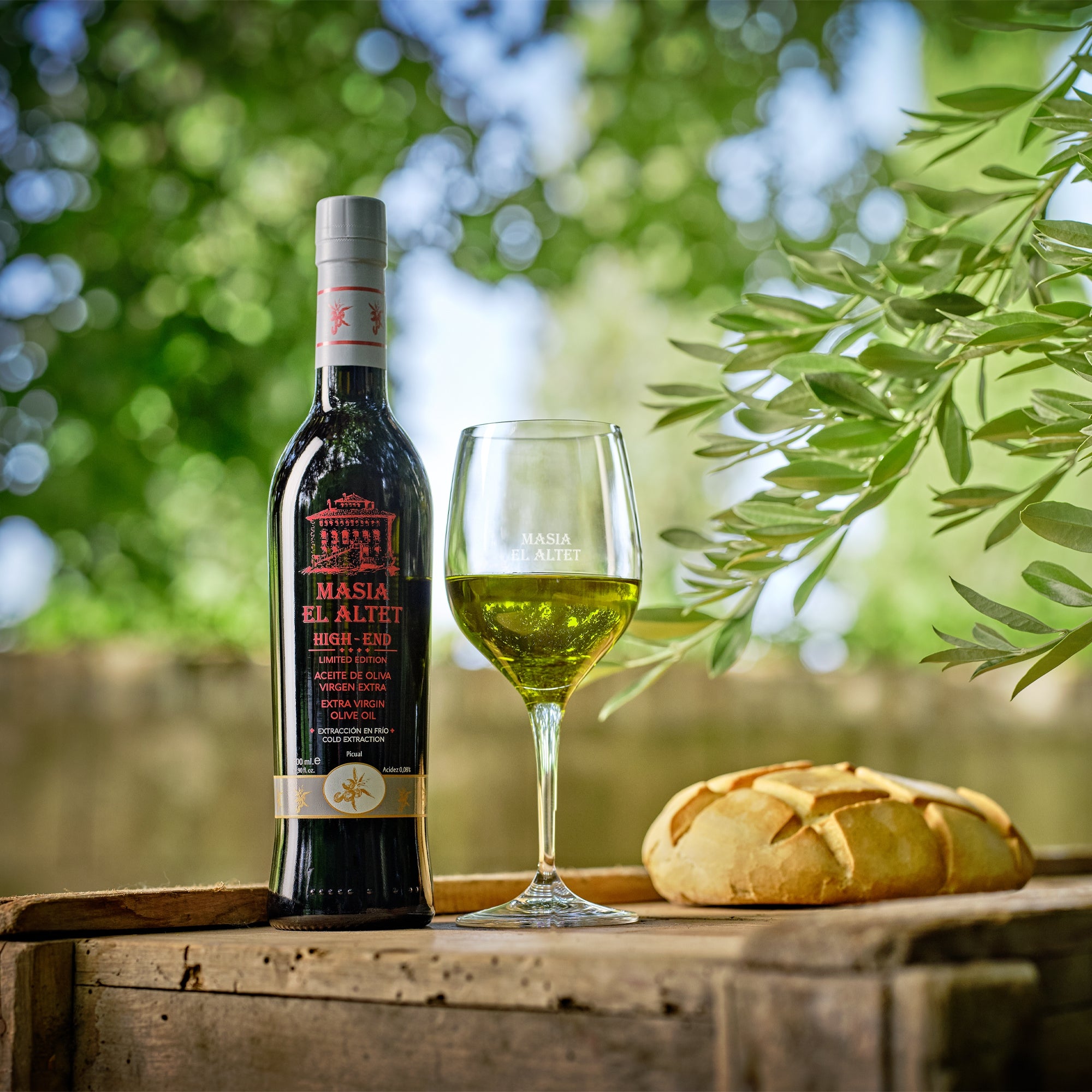 A 500 ml bottle of Masia el Altet High End beside a bread, and a glass with olive oil.