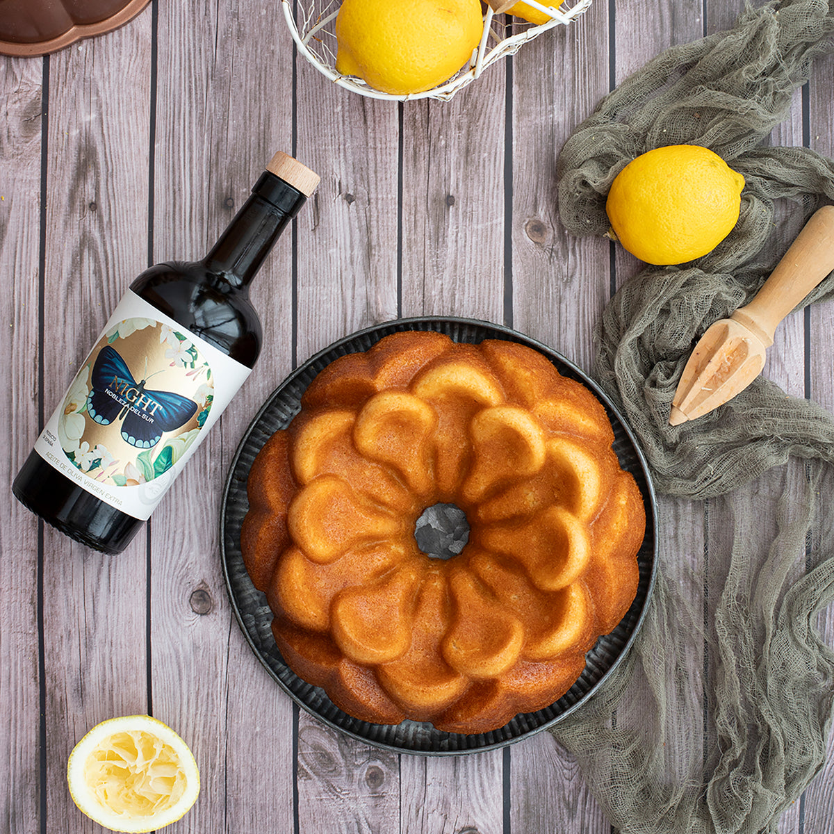 Nobleza del Sur Organic Night beside a lemon cake, fresh lemons, and a wooden citrus juicer.