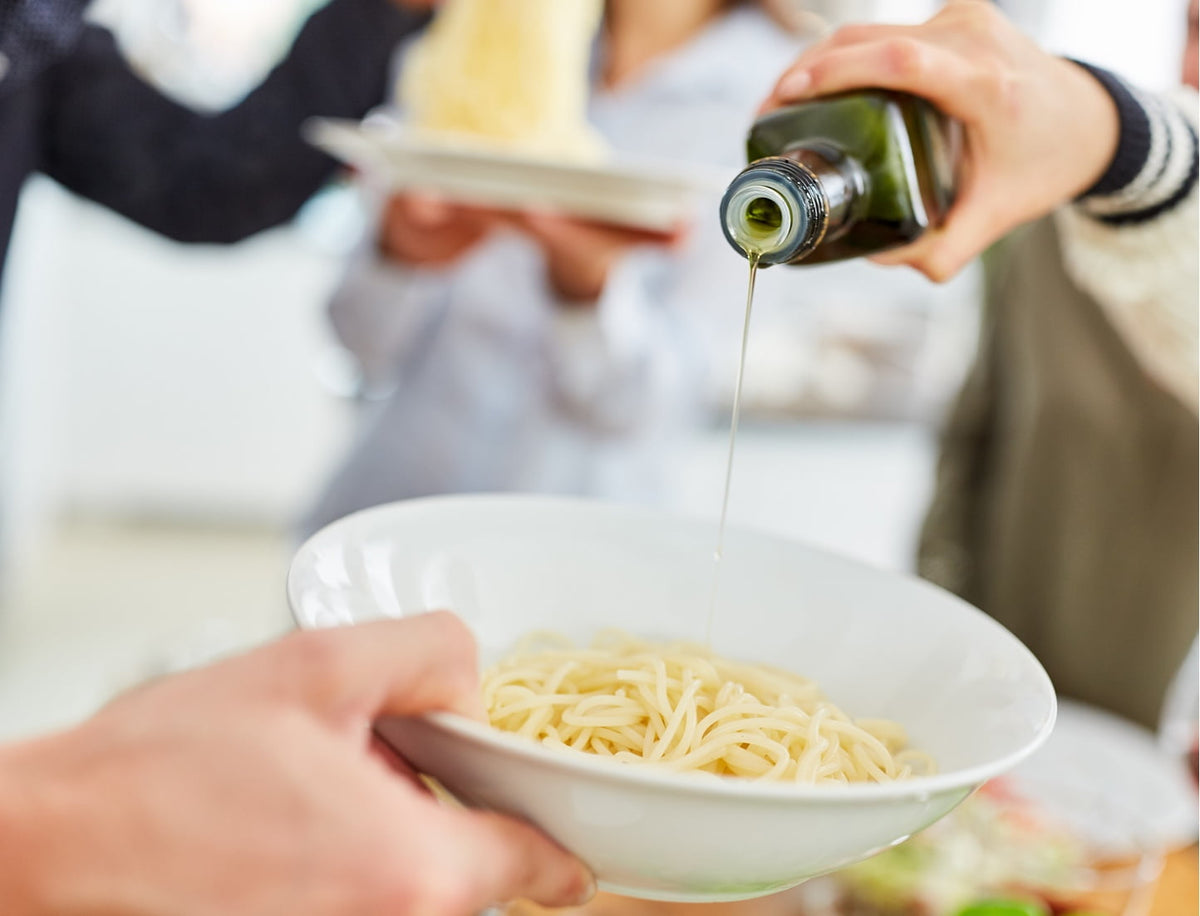 Olive oil being poured over pasta.