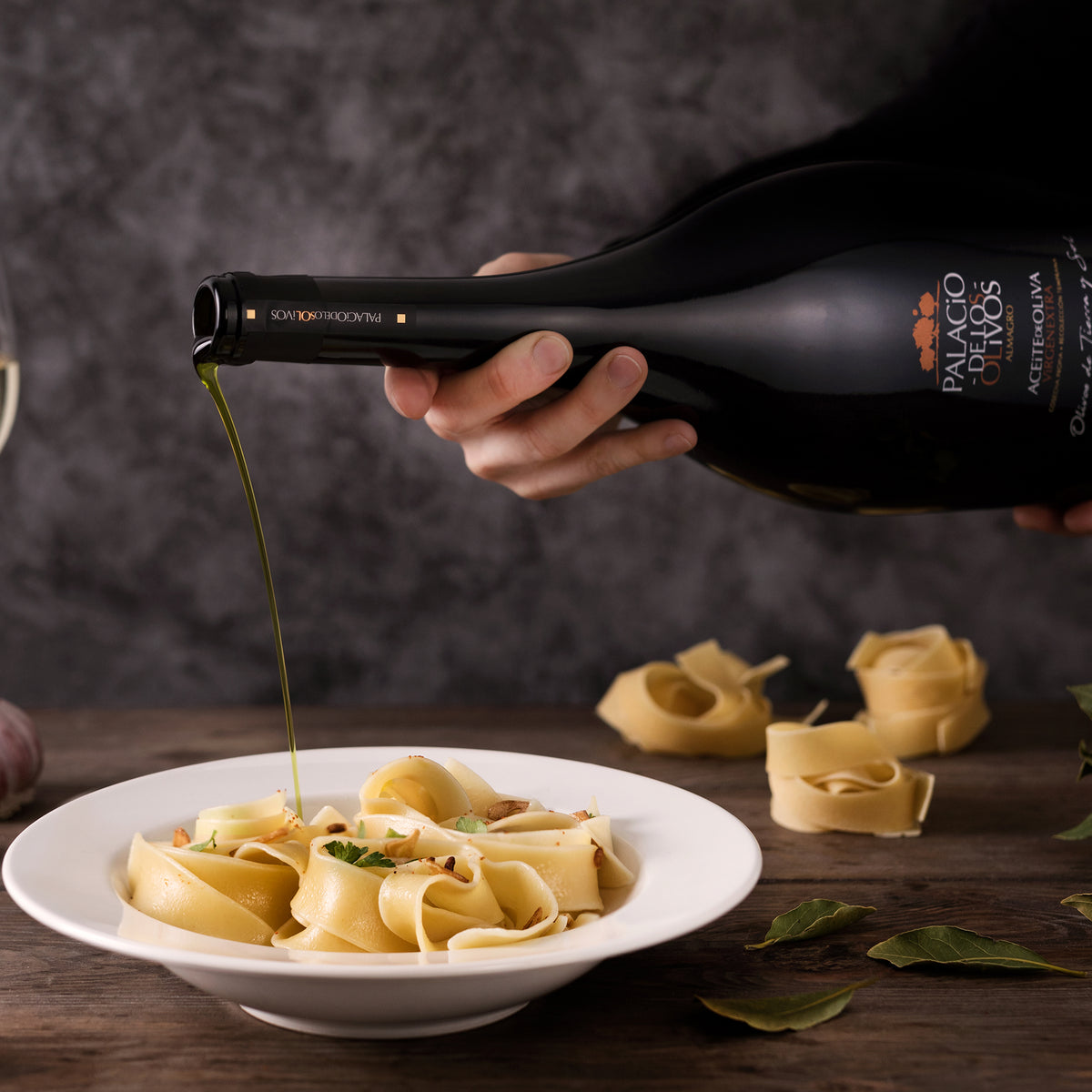 Palacio de los Olivos Picual Magnum bottle pouring green olive oil over a plate of ribbon pasta.