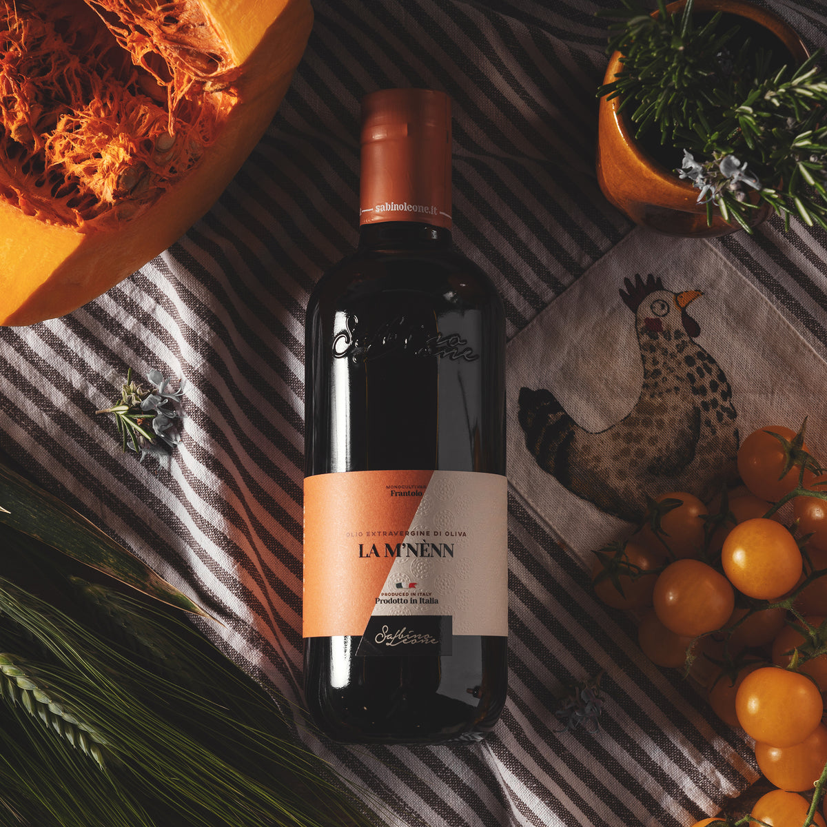 A Sabino Leone La M'Nenn 500 ml bottle with pumpkin, yellow tomatoes, rosemary, and wheat.