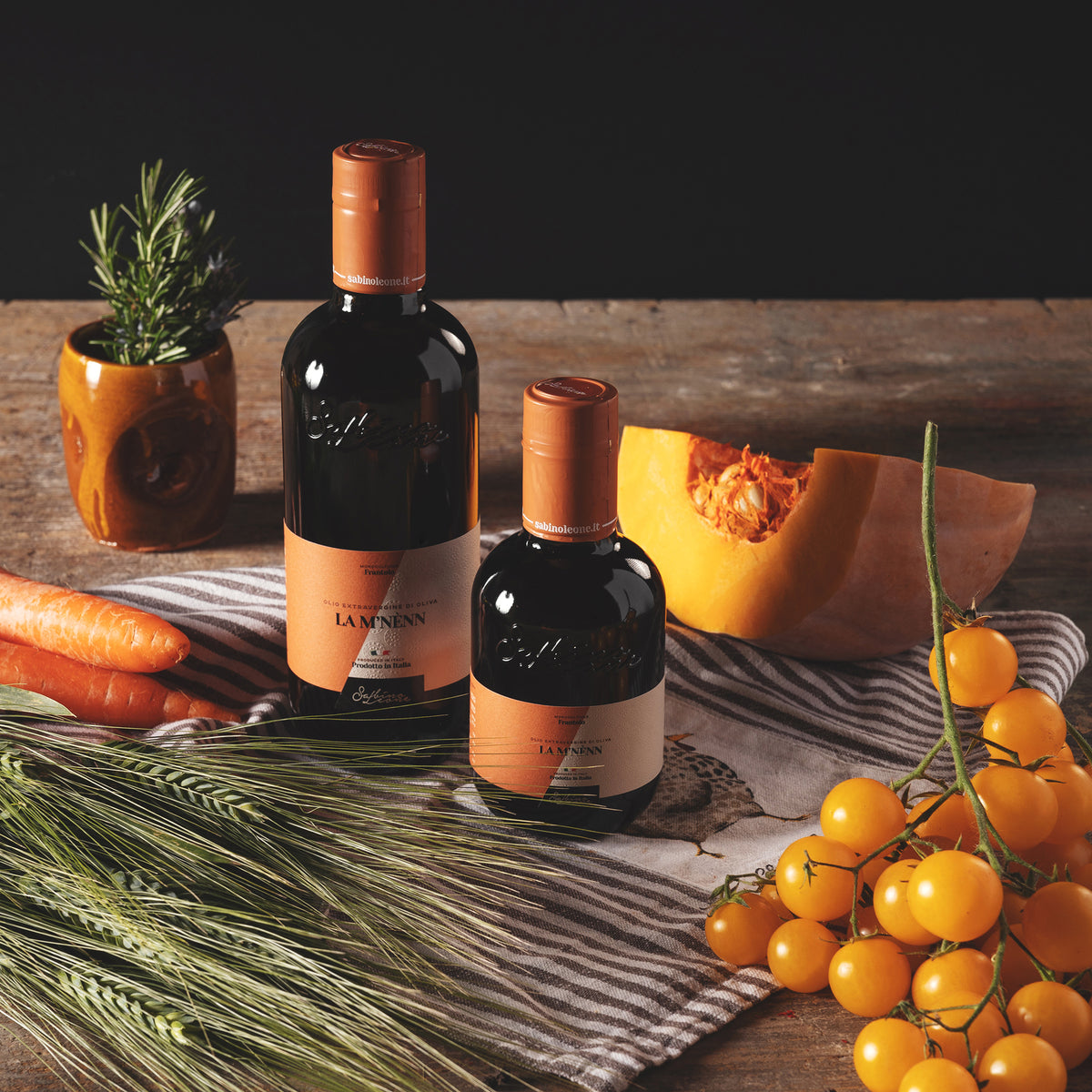 Sabino Leone La M'Nenn bottles beside pumpkin, carrots, tomatoes, rosemary, and wheat.