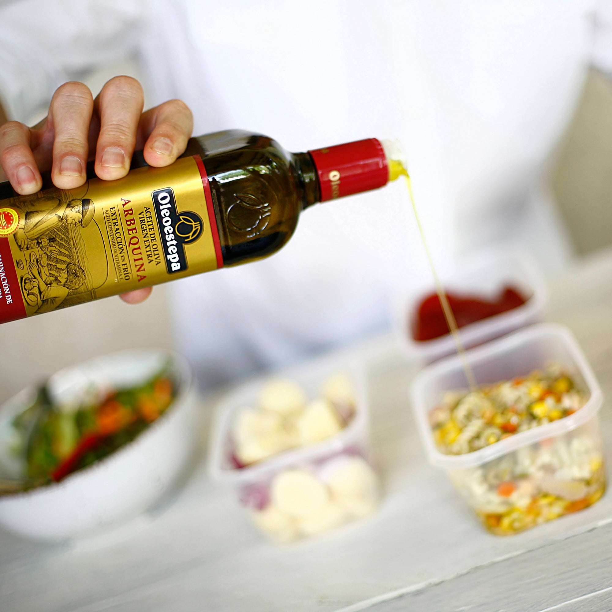 Oleoestepa Arbequina extra virgin olive oil being poured over a prepared dish in a food container.