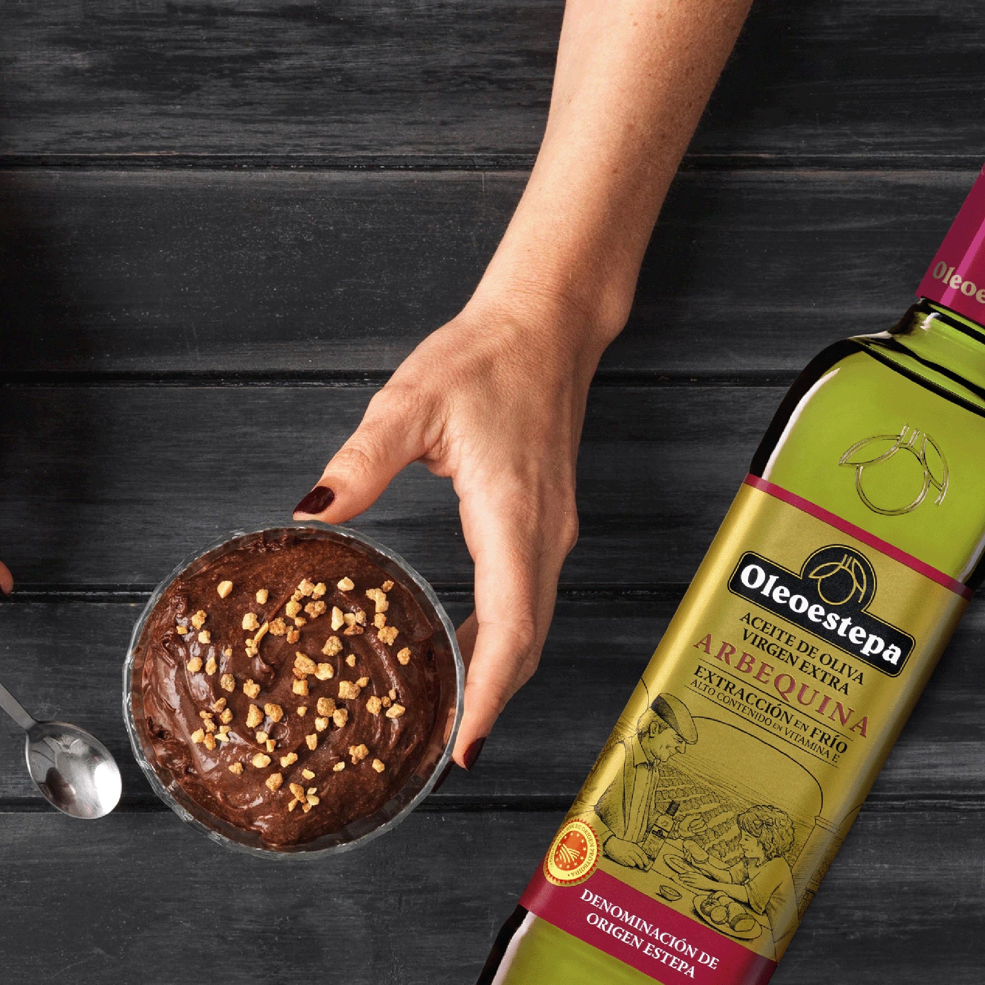 Oleoestepa Arbequina bottle beside a bowl of chocolate dessert topped with crunchy pieces.