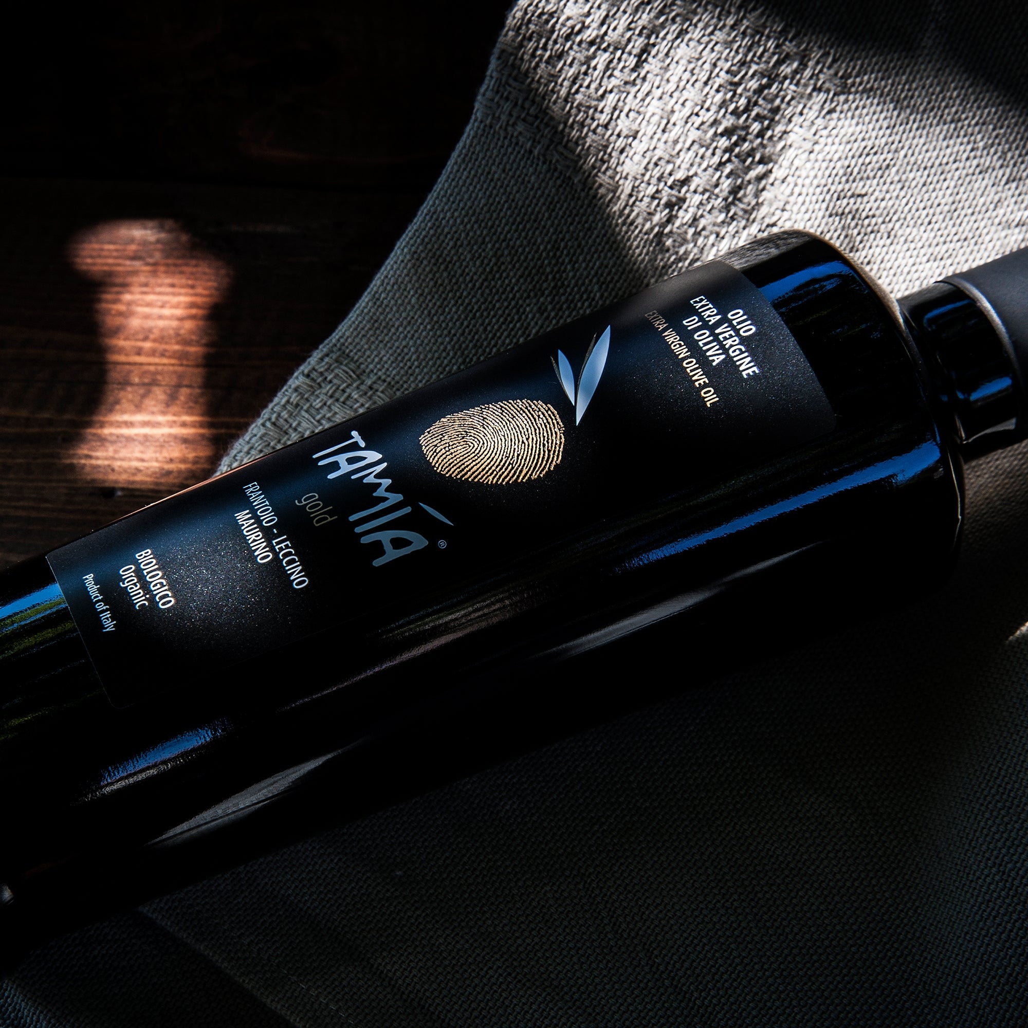 Close-up of a Tamia Gold Organic 500 ml olive oil bottle on fabric.