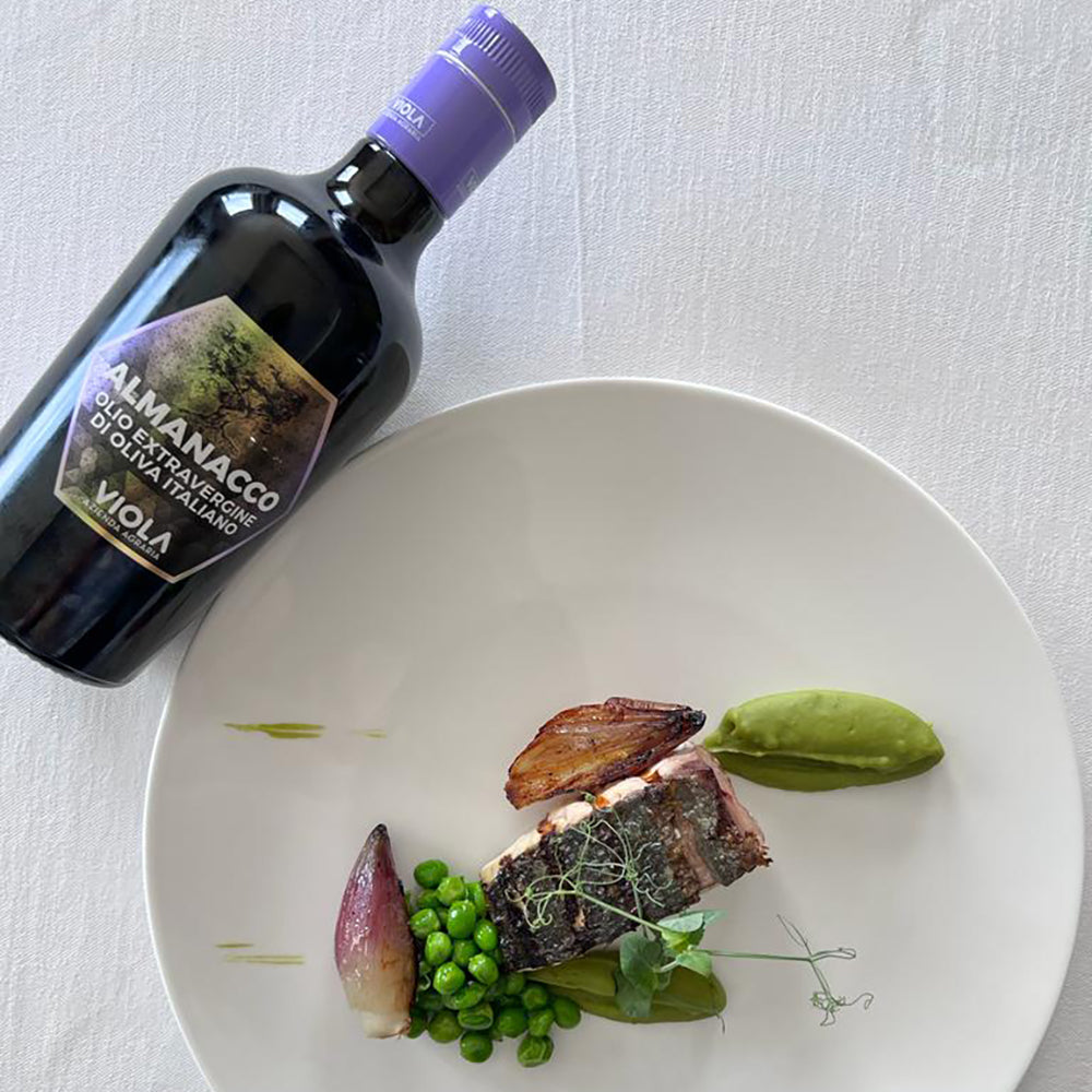 Viola Almanacco Centennial extra virgin olive oil beside a plated gourmet dish with fish, and peas.