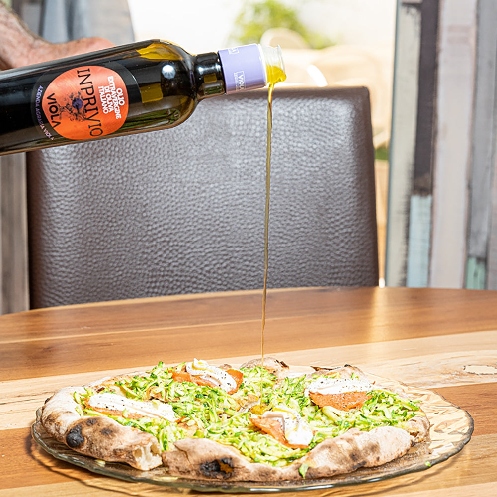 Viola Inprivio olive oil being poured over a freshly prepared pizza.