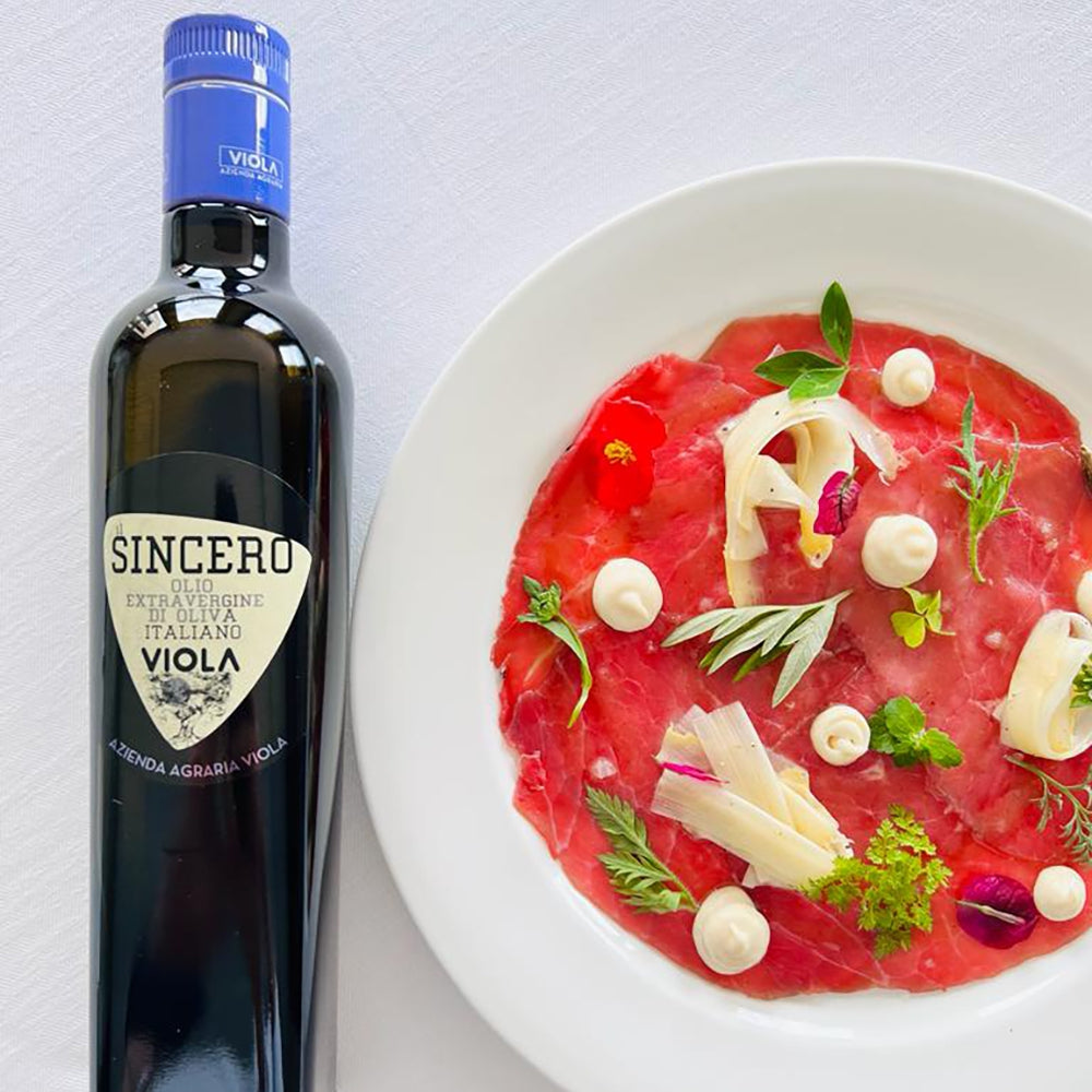 Viola Il Sincero bottle beside beef carpaccio garnished with cheese, herbs, and edible flowers.