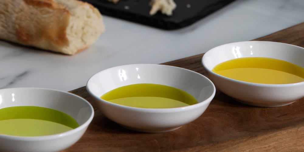 Three bowls with olive oils ranging from vivid green to golden, with bread nearby.