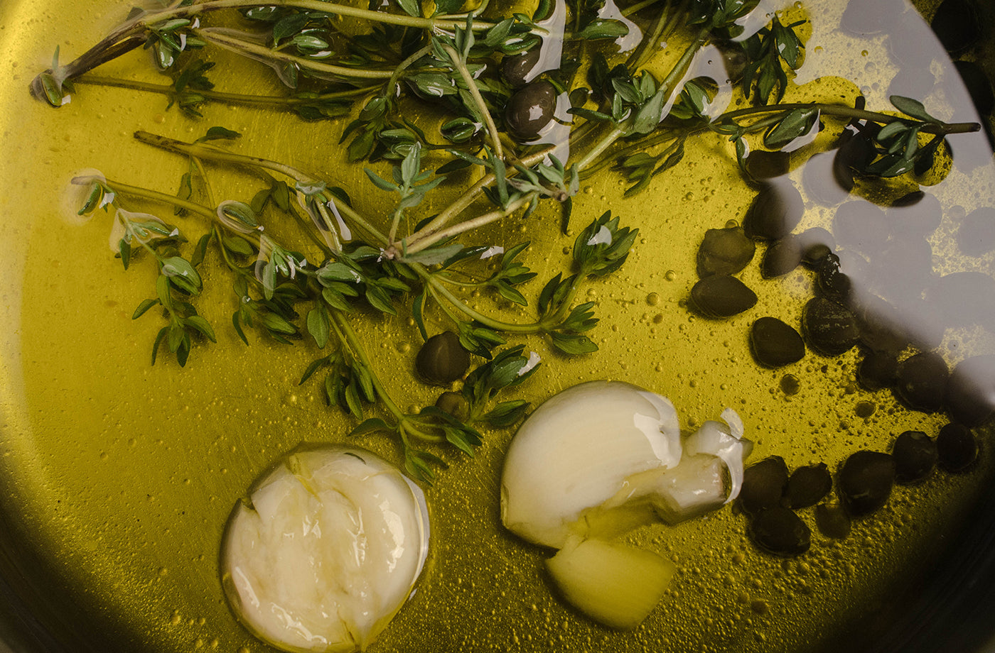 Herbs and garlic cloves on a pan with extra virgin olive oil.