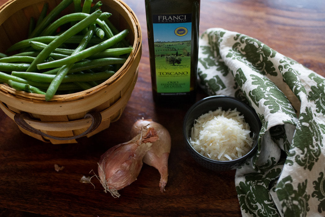 A bottle of Franci IGP Toscano extra virgin olive oil on a table, alongside green beans, onions, and rice.