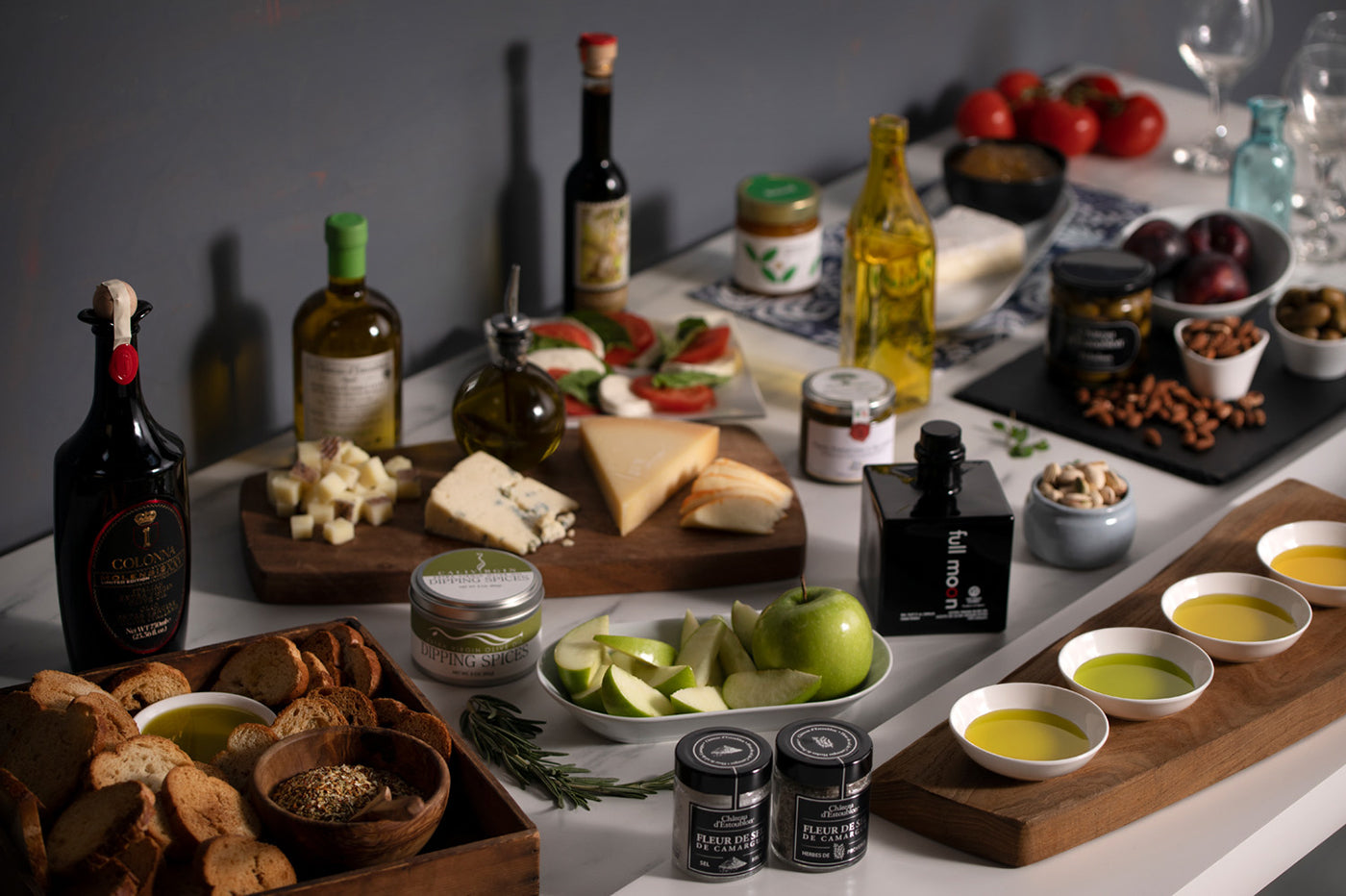 A table featuring an assortment of food items, including extra virgin olive oils available at Olive Oil Lovers, bread, cheese, and fresh fruit.
