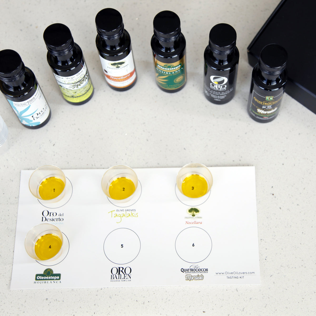 Six olive oils and four tasting cups arranged on a tasting mat.