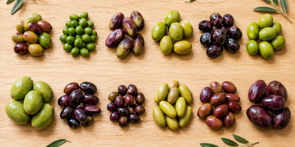 Green, purple, and black olive varieties arranged in groups on a wooden surface.